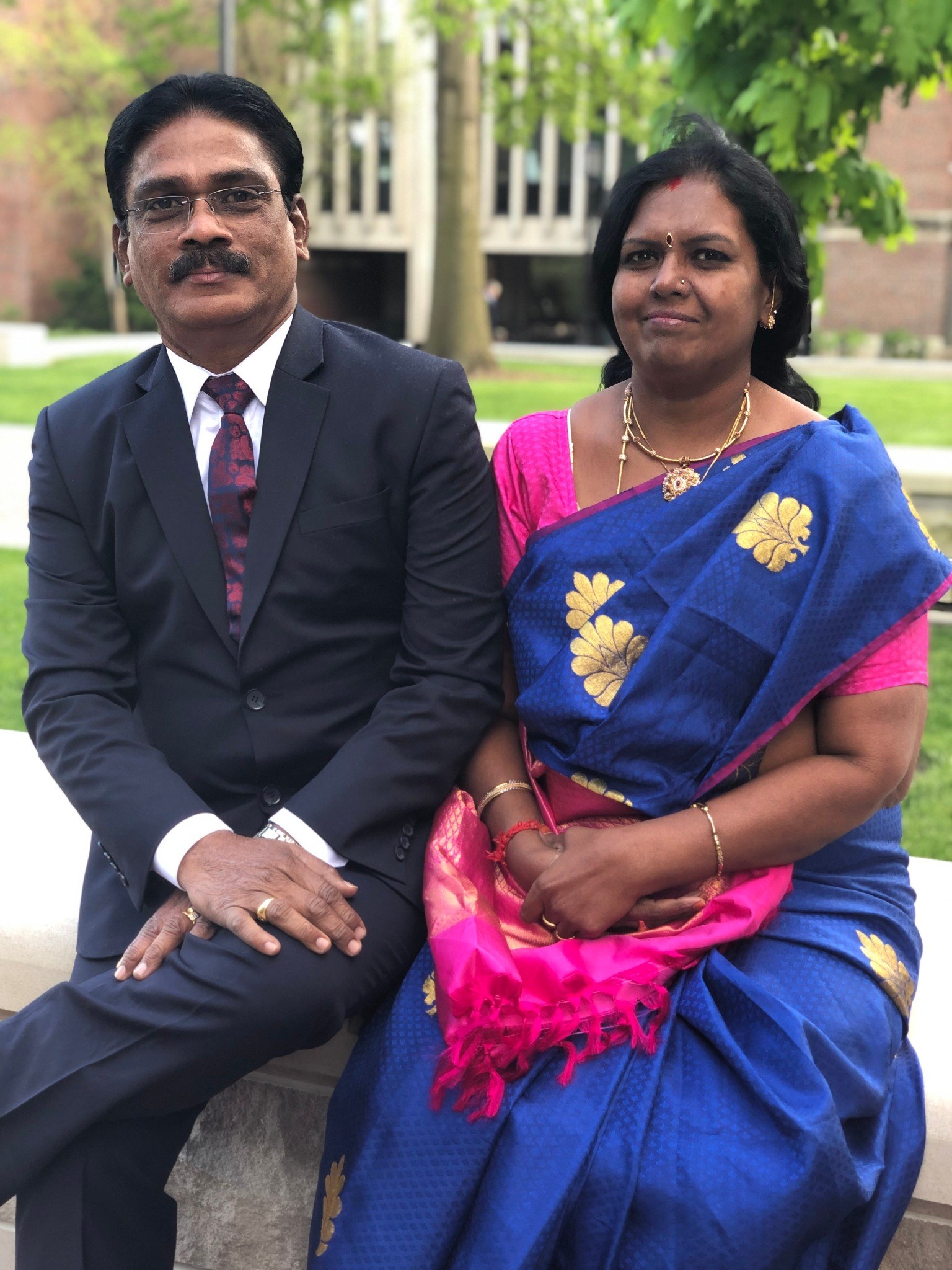 Venkatesan and Devi seated together outdoors on a university campus in the United States.